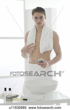 Stock Photography - Man standing in front of a washbowl holding a small perfume bottle. Fotosearch