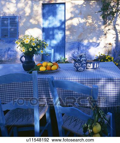 Stock Image - Blue and white table with lemons and oranges and a bouquet of marguerites. Fotosearch
