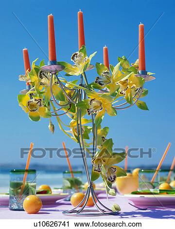 Stock Image - Candles and cymbidium blossom on a summery table. Fotosearch