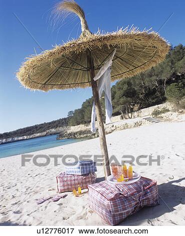 Stock Photo - On the beach: beach bag and soft drinks under a parasol made of straw. Fotosearch