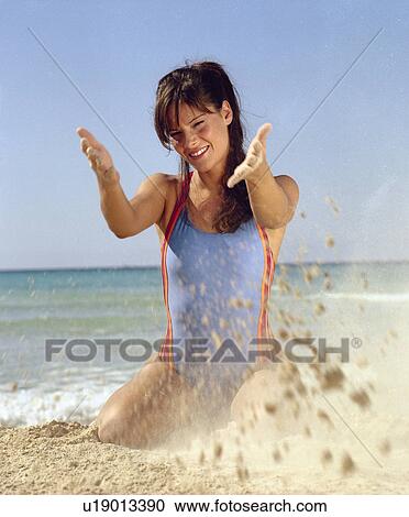 Stock Image - Woman in swimsuit playing with sand. Fotosearch