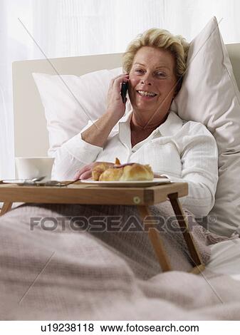 Stock Photo - elderly lady with her mobile in bed. Fotosearch