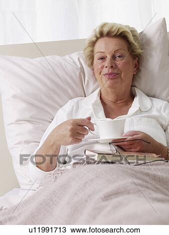 Stock Image - senior lady having a cup of coffee in bed. Fotosearch