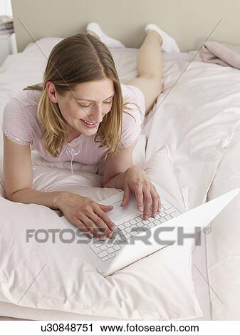 Stock Image - young woman with her laptop in bed. Fotosearch