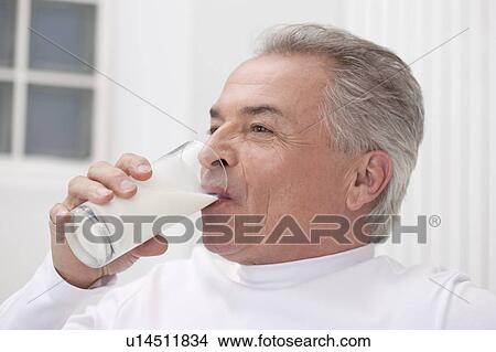 Picture - Domestic Life, a senior man drinking a glass of milk and looking away. Fotosearch
