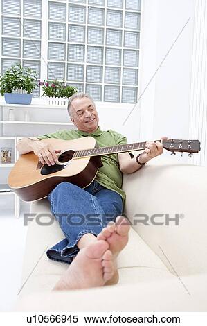 Stock Photography - Domestic Life, a senior man lying on sofa and playing guitar. Fotosearch