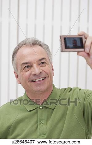 Stock Photo - Domestic Life, a senior man taking picture of himself and smiling. Fotosearch