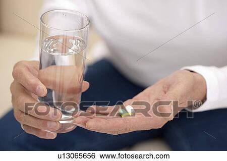 Stock Photograph - Domestic Life, a senior man taking medicine with a glass of water. Fotosearch