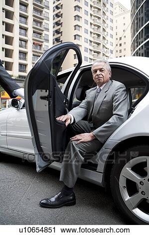 Stock Image - Senior businessman getting off the car and looking at the camera. Fotosearch