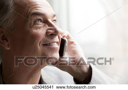 Stock Image - Senior businessman holding mobile phone and looking up with smile. Fotosearch
