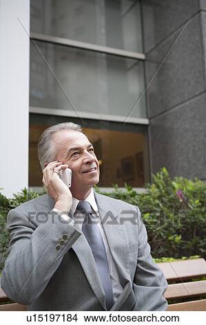 Picture - Senior businessman sitting and using mobile phone with smile. Fotosearch