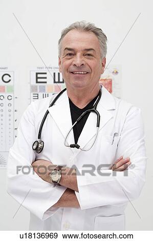 Stock Photo - Senior doctor standing with arms crossed and smiling at the camera. Fotosearch