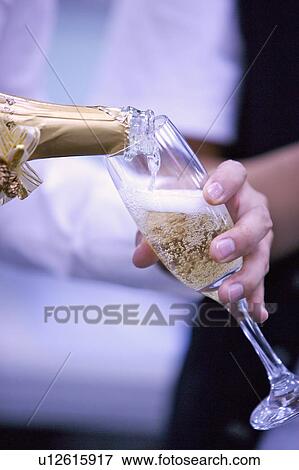 Stock Photo - Close-up of people pouring champagne into a glass. Fotosearch