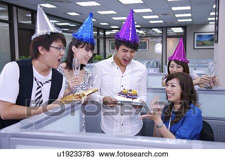 Stock Image - Colleagues wearing headwear and holding a cake for celebrating. Fotosearch