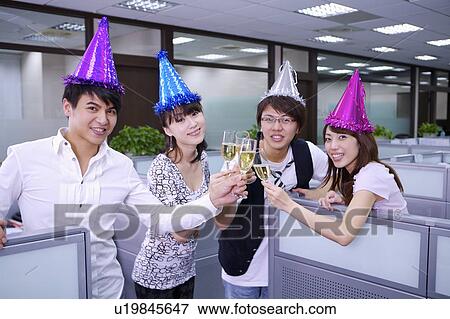 Stock Photo - Four colleagues wearing headwear and toasting with smile. Fotosearch