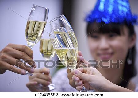 Stock Image - People holding glasses of champagne to toast together. Fotosearch