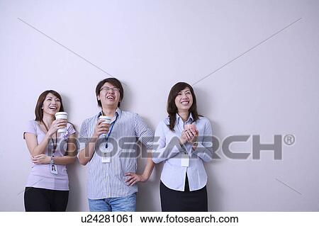 Stock Image - Three colleagues holding coffee and smiling happily together. Fotosearch