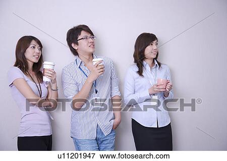 Stock Photo - Three colleagues holding drinks and looking up with smile together. Fotosearch