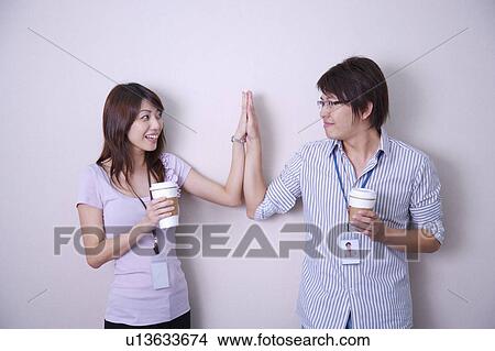 Young man and woman holding coffee together and making high-five View Large Photo Image Picture - Young man and woman holding coffee together and making high-five. Fotosearch