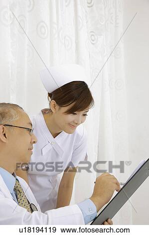 Stock Photo - Doctor and nurse looking at the clipboard together with smile. Fotosearch