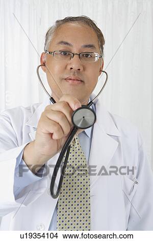 Doctor holding stethoscope and looking at the camera View Large Photo Image Picture - Doctor holding stethoscope and looking at the camera. Fotosearch
