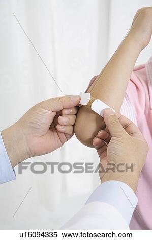 Stock Photography - Doctor putting adhesive bandage on patient's arm. Fotosearch