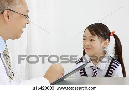 Stock Image - Doctor talking with little girl and writing on clipboard. Fotosearch