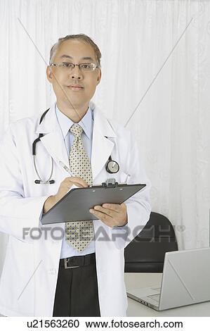 Doctor writing on clipboard and looking at the camera View Large Photo Image Stock Image - Doctor writing on clipboard and looking at the camera. Fotosearch