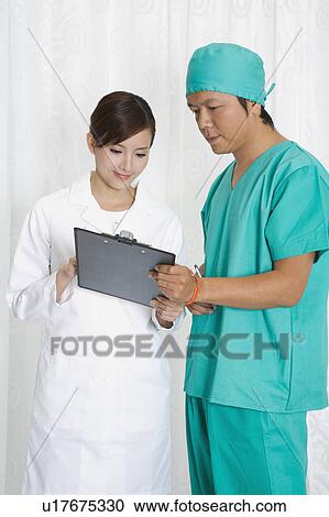Stock Image - Female doctor and surgeon looking at the clipboard together. Fotosearch