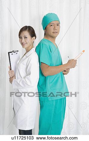 Stock Image - Female doctor and surgeon standing with back to back and looking at the camera. Fotosearch