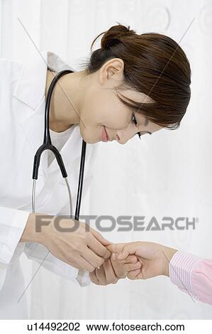 Stock Image - Female doctor checking patient's hand. Fotosearch