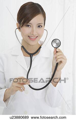 Stock Photo - Female doctor holding stethoscope and looking at the camera with smile. Fotosearch