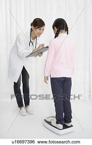 Stock Photograph - Female doctor writing on clipboard of little girl's weight. Fotosearch