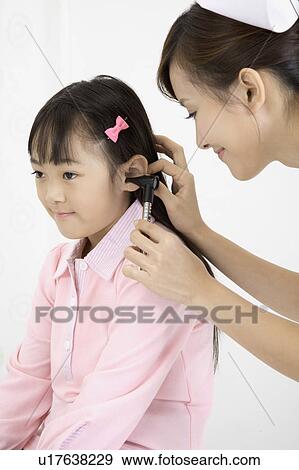 Young nurse checking little girl's ear with medical equipment View Large Photo Image Stock Photo - Young nurse checking little girl's ear with medical equipment. Fotosearch