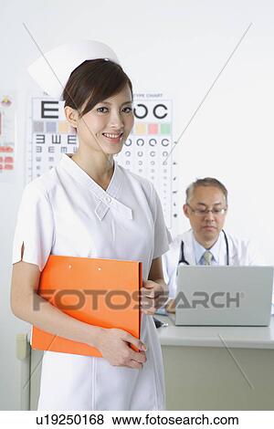 Stock Photo - Young nurse holding document folder and smiling at the camera. Fotosearch
