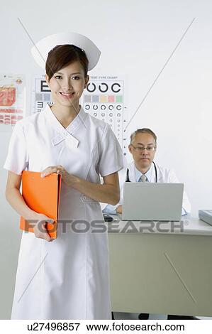Stock Photo - Young nurse holding document folder and smiling at the camera. Fotosearch