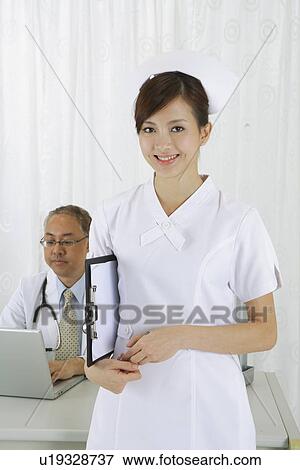 Stock Photo - Young nurse standing with clipboard and smiling at the camera. Fotosearch