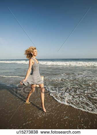 Stock Photo - Attractive young woman walking on sandy beach. Fotosearch
