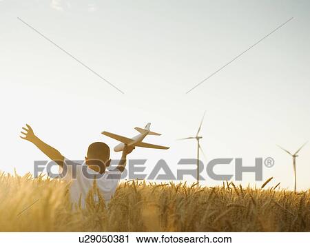 Stock Image - Boy (10-11) playing with toy aeroplane in wheat field. Fotosearch