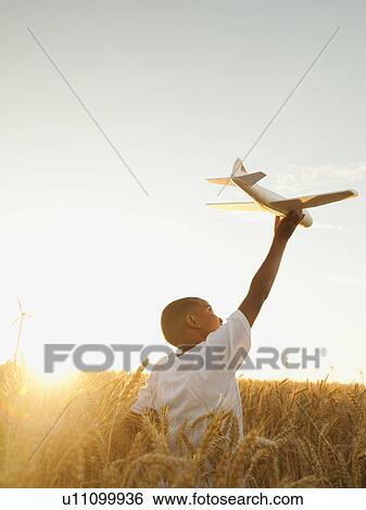 Stock Photograph - Boy (10-11) playing with toy aeroplane in wheat field. Fotosearch