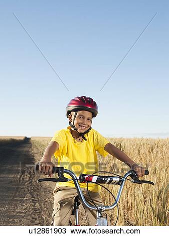 Stock Image - Boy (8-9) cycling along dirt road. Fotosearch