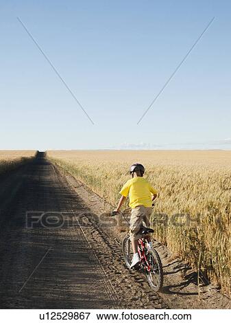 Stock Photo - Boy (8-9) cycling along dirt road. Fotosearch