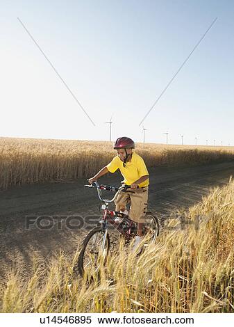 Boy (8-9) cycling along dirt road View Large Photo Image Stock Photography - Boy (8-9) cycling along dirt road. Fotosearch