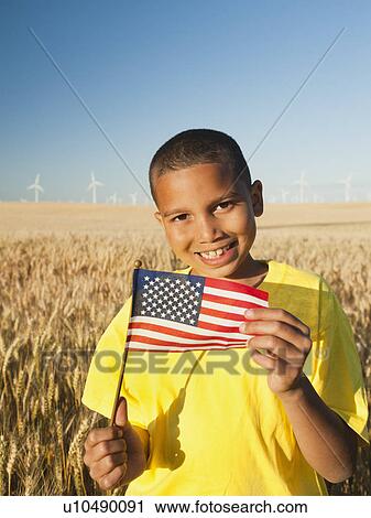 Stock Image - Boy (8-9) holding a small American flag in wheat field. Fotosearch
