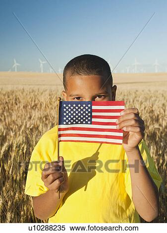 Boy (8-9) holding a small American flag in wheat field View Large Photo Image Stock Photography - Boy (8-9) holding a small American flag in wheat field. Fotosearch
