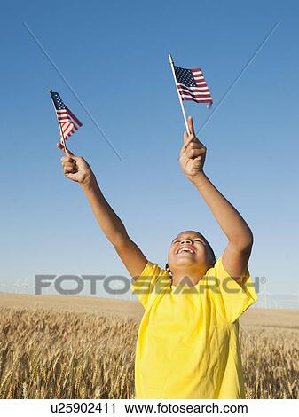 Stock Image - Boy (8-9) holding small american flags in wheat field. Fotosearch