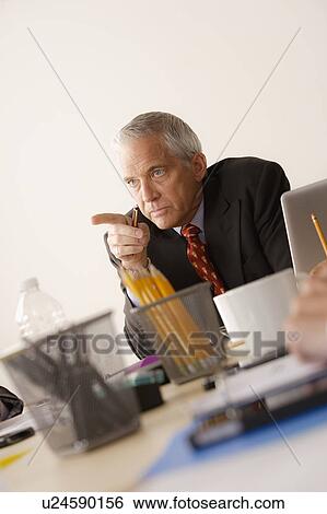 Stock Photograph - Businessman pointing finger from behind desk. Fotosearch