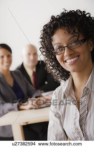 Picture - Businesswoman looking at camera, business team in background. Fotosearch