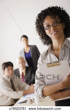 Stock Image - Businesswoman looking at camera, business team in background. Fotosearch
