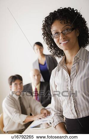 Stock Photography - Businesswoman looking at camera, business team in background. Fotosearch